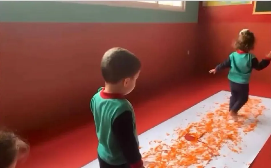 Niños pintando con los pies sobre papel continuo, actividad de psicomotricidad